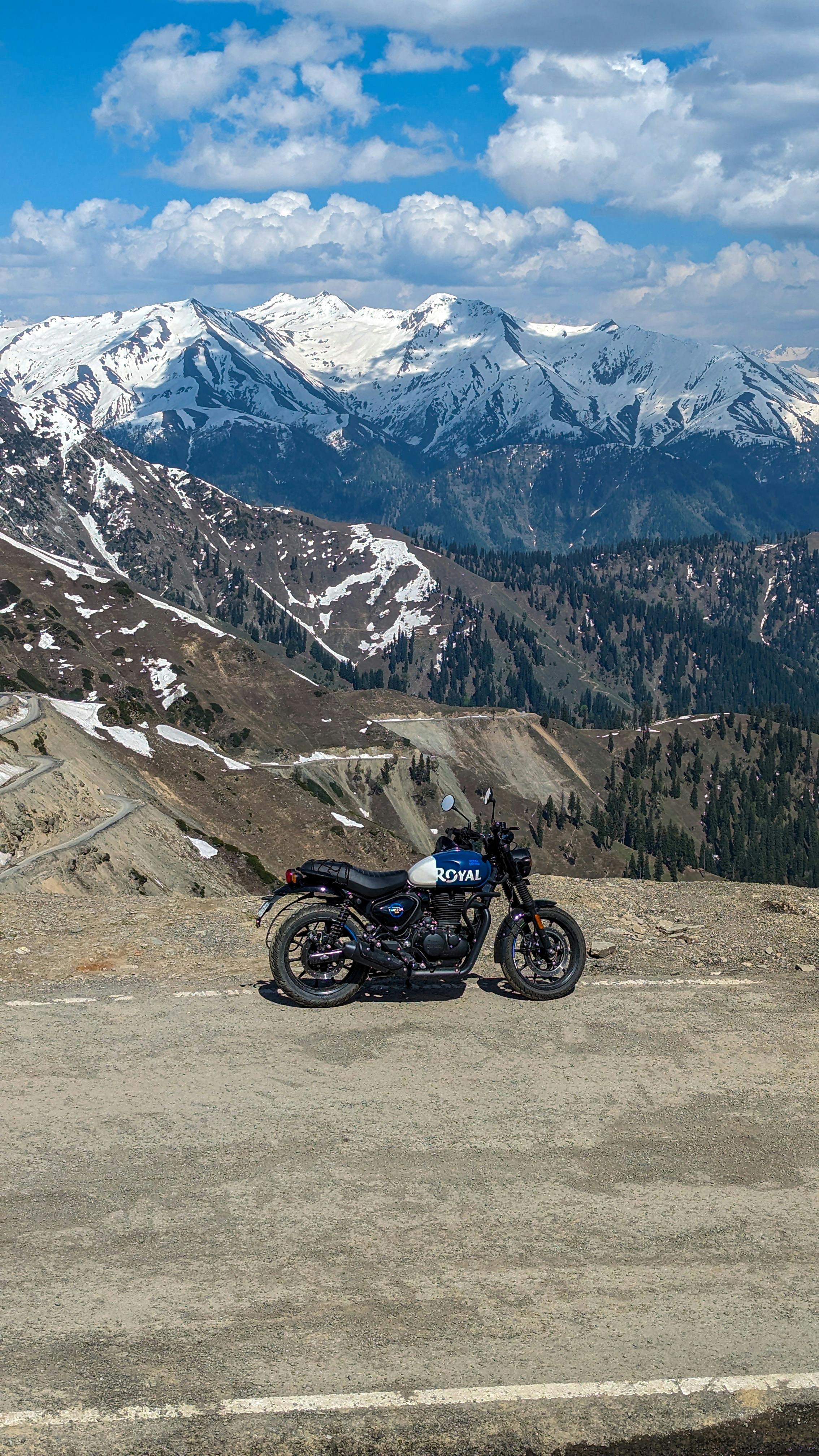 Motorcycle on a mountain pass with snow-capped peaks and winding roads, perfect for adventurous travel.