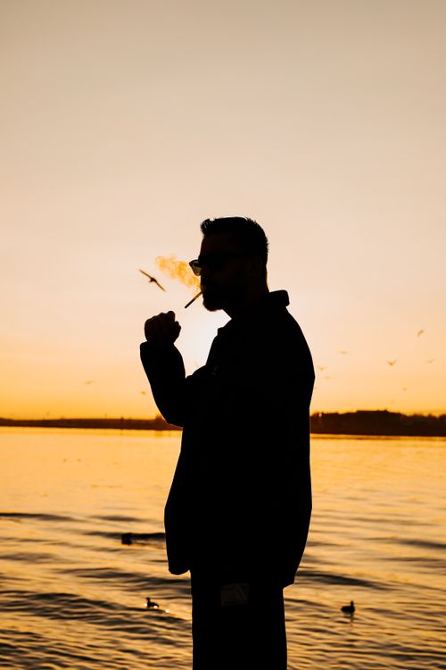 Silhouette of Man Smoking by the Lake at Sunset · Free Stock Photo