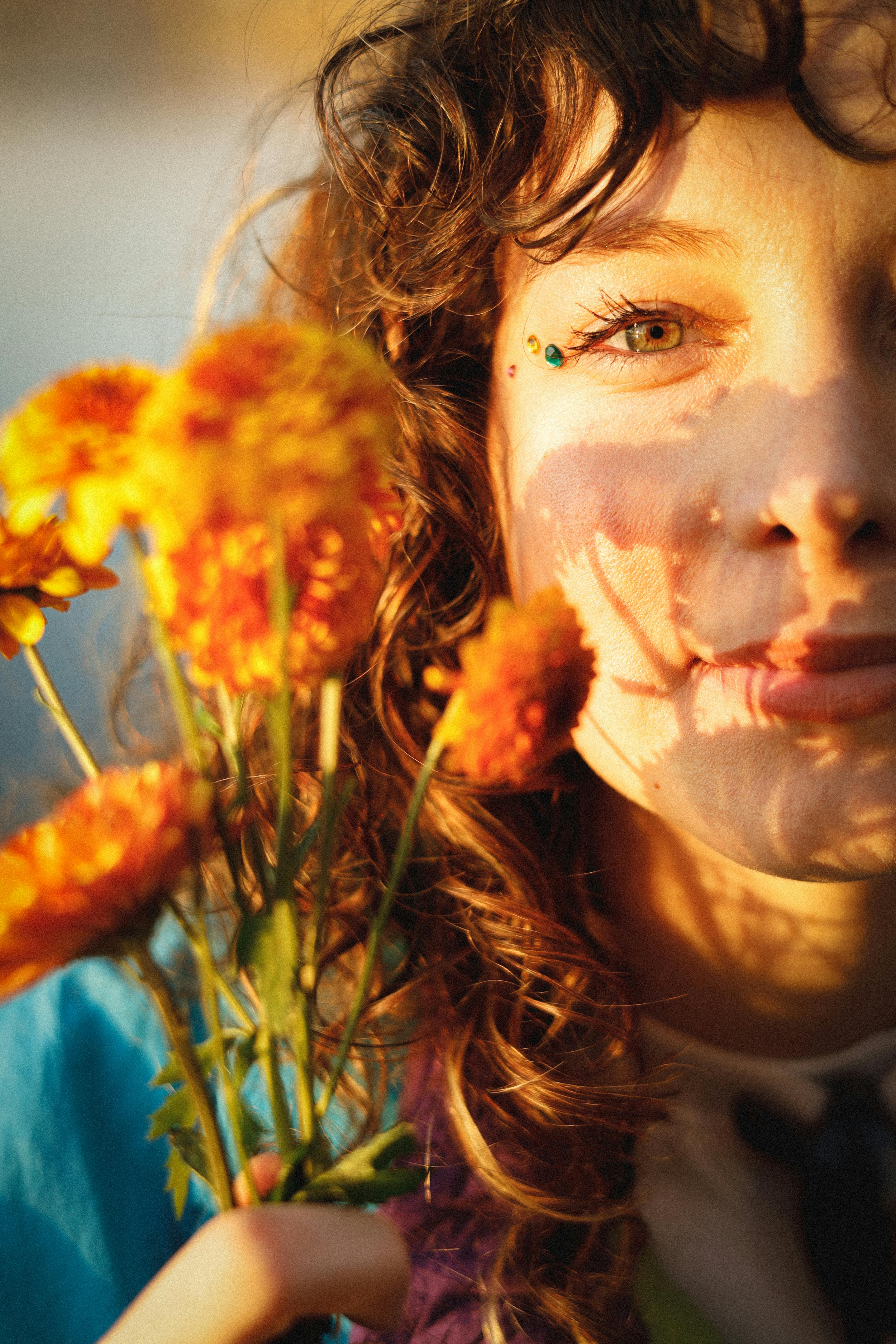 Portrait of a young woman holding orange flowers in warm sunlight, casting shadows on her face.