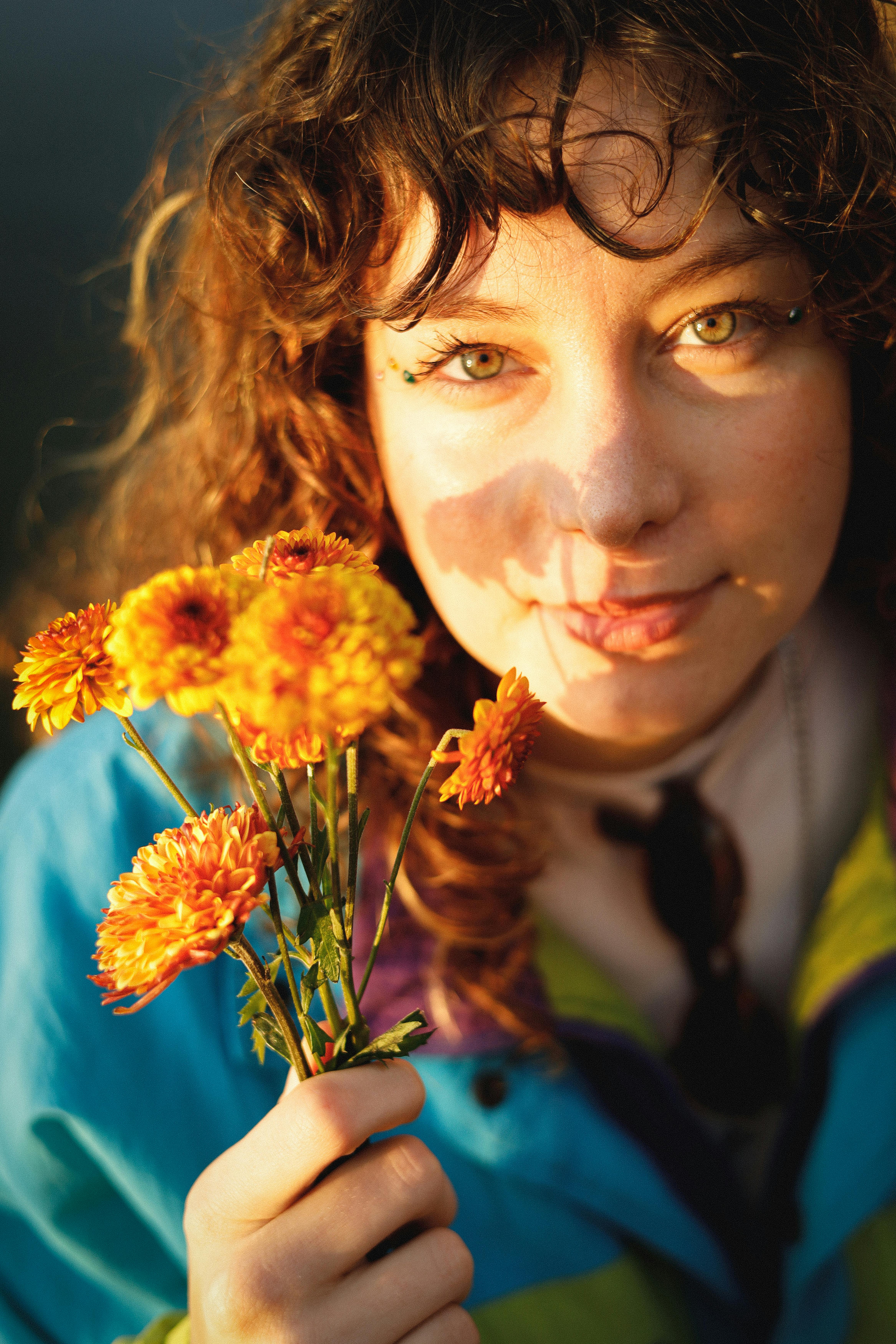 A young woman holds vibrant marigold flowers, illuminated by warm, natural light.