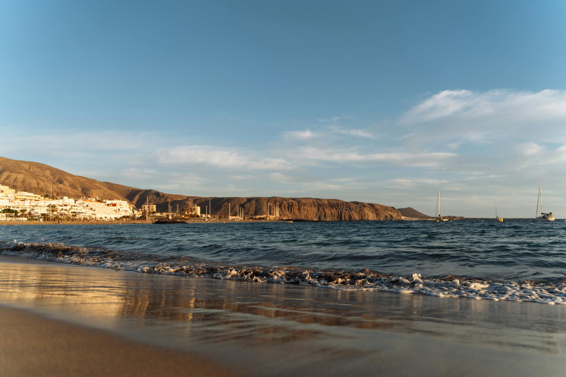Peaceful beachfront view in the Canary Islands with sailboats and golden sunset light.