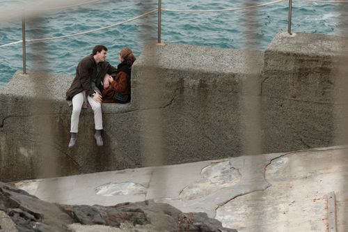 Free A couple enjoys a quiet moment seated by a seaside barrier overlooking the ocean. Stock Photo
