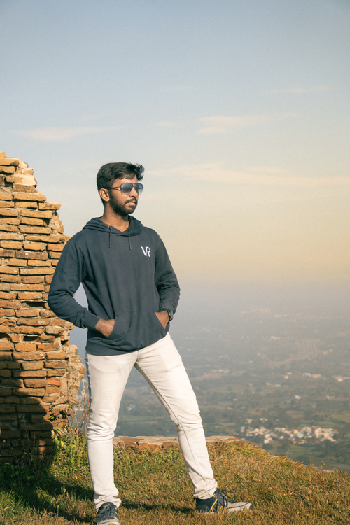 Free Young man in sunglasses and hoodie standing by ancient ruins overlooking a scenic landscape. Stock Photo