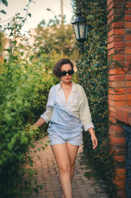 Woman wearing sunglasses walking in lush brick-lined garden, Ciudad del Este