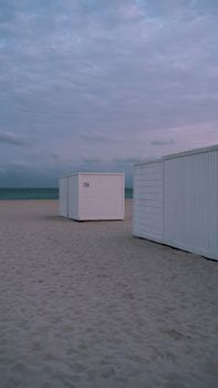Quiet beach scene with white cabins during twilight, offering a serene seaside atmosphere.