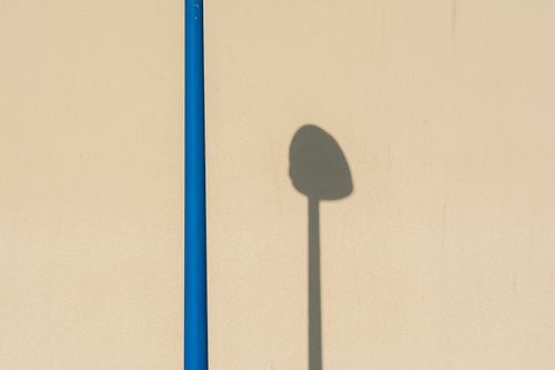 Free Minimalist composition of a street light shadow on a beige wall with vivid blue pole contrast. Stock Photo