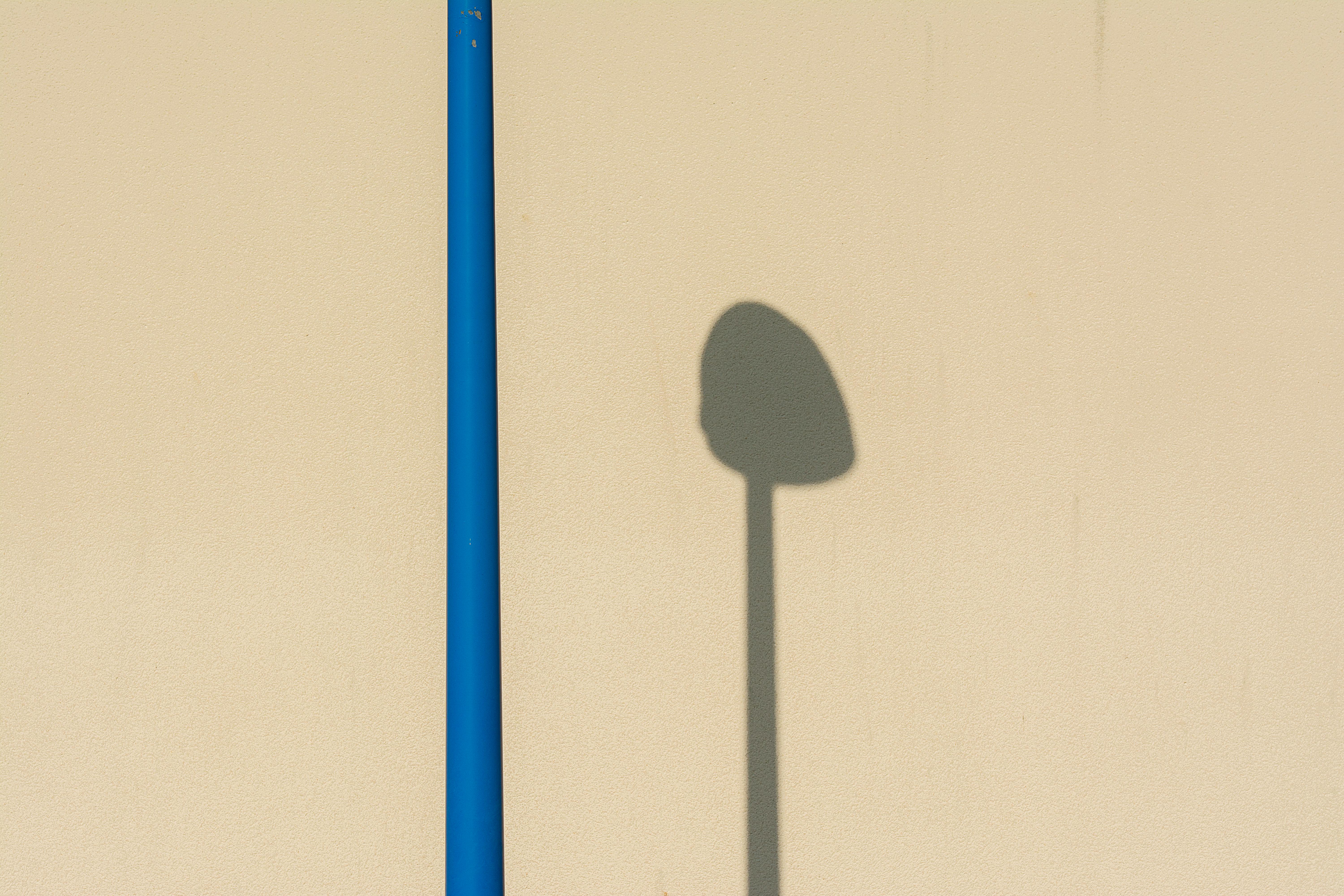 grátis Composição minimalista de uma sombra de iluminação pública em uma parede bege com contraste de um poste azul vivo. Foto profissional