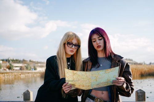 Free Two young women explore nature holding a map, planning their journey under a bright sky. Stock Photo