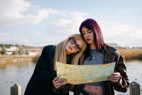 Free Two young women exploring with a map by a lake, looking for directions in a natural setting. Stock Photo