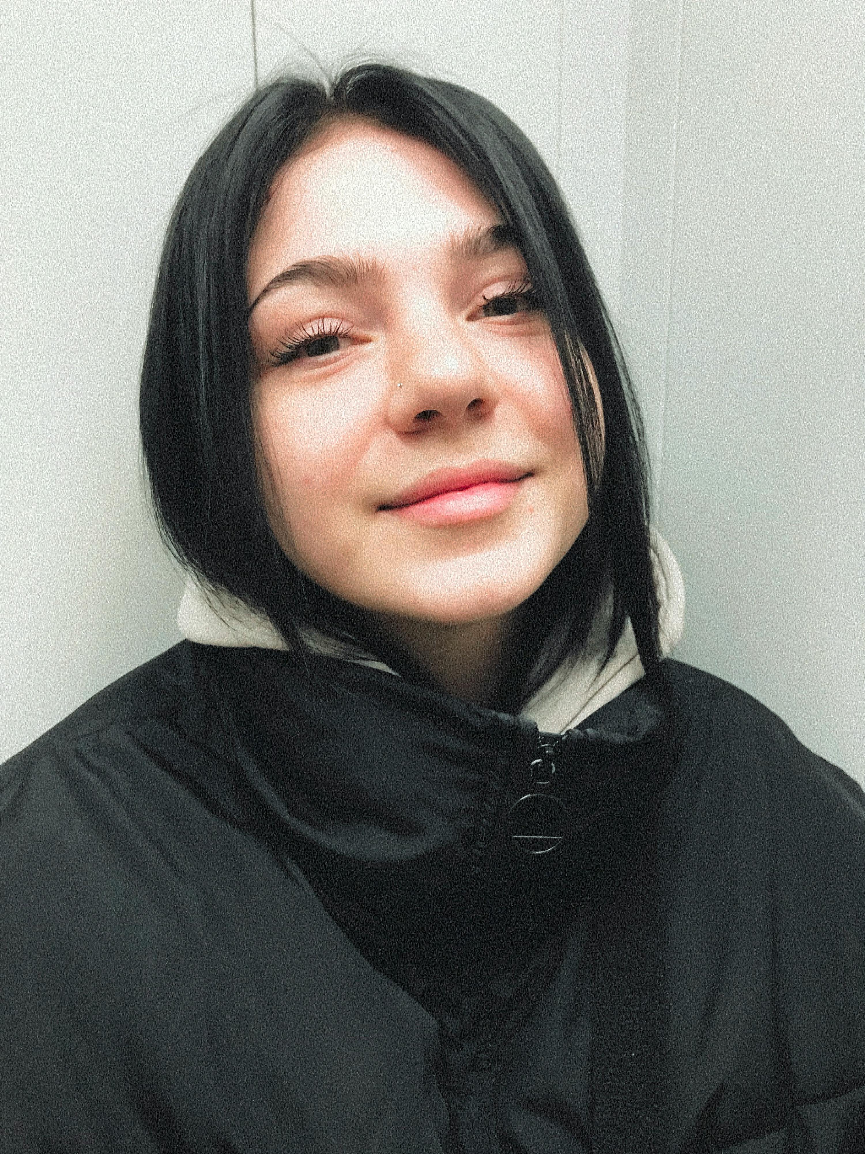 Portrait of a young woman warmly dressed in a coat indoors. Soft lighting enhances her smile.