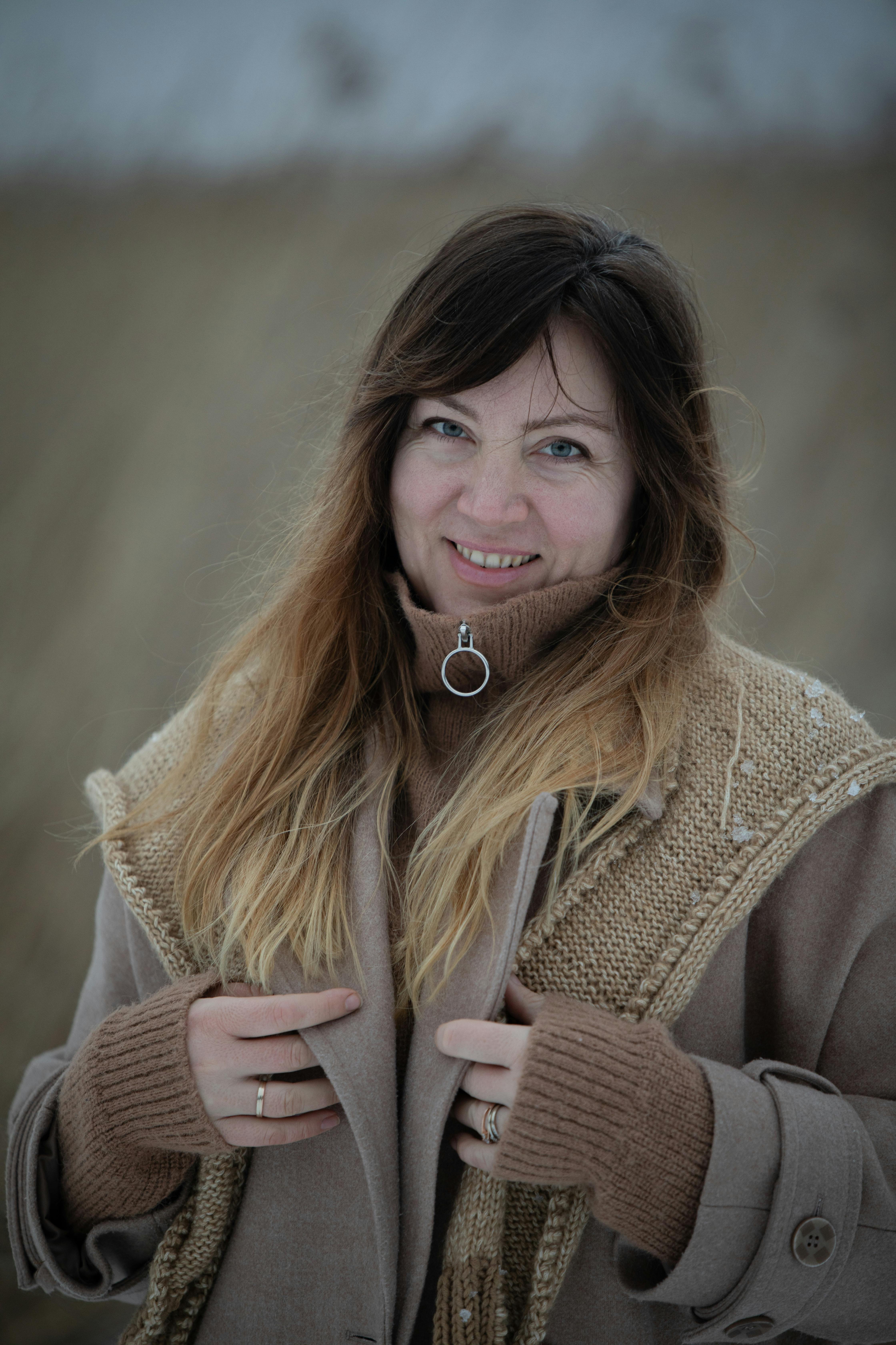 Woman wearing a wool coat and scarf outdoors, smiling in a winter setting.