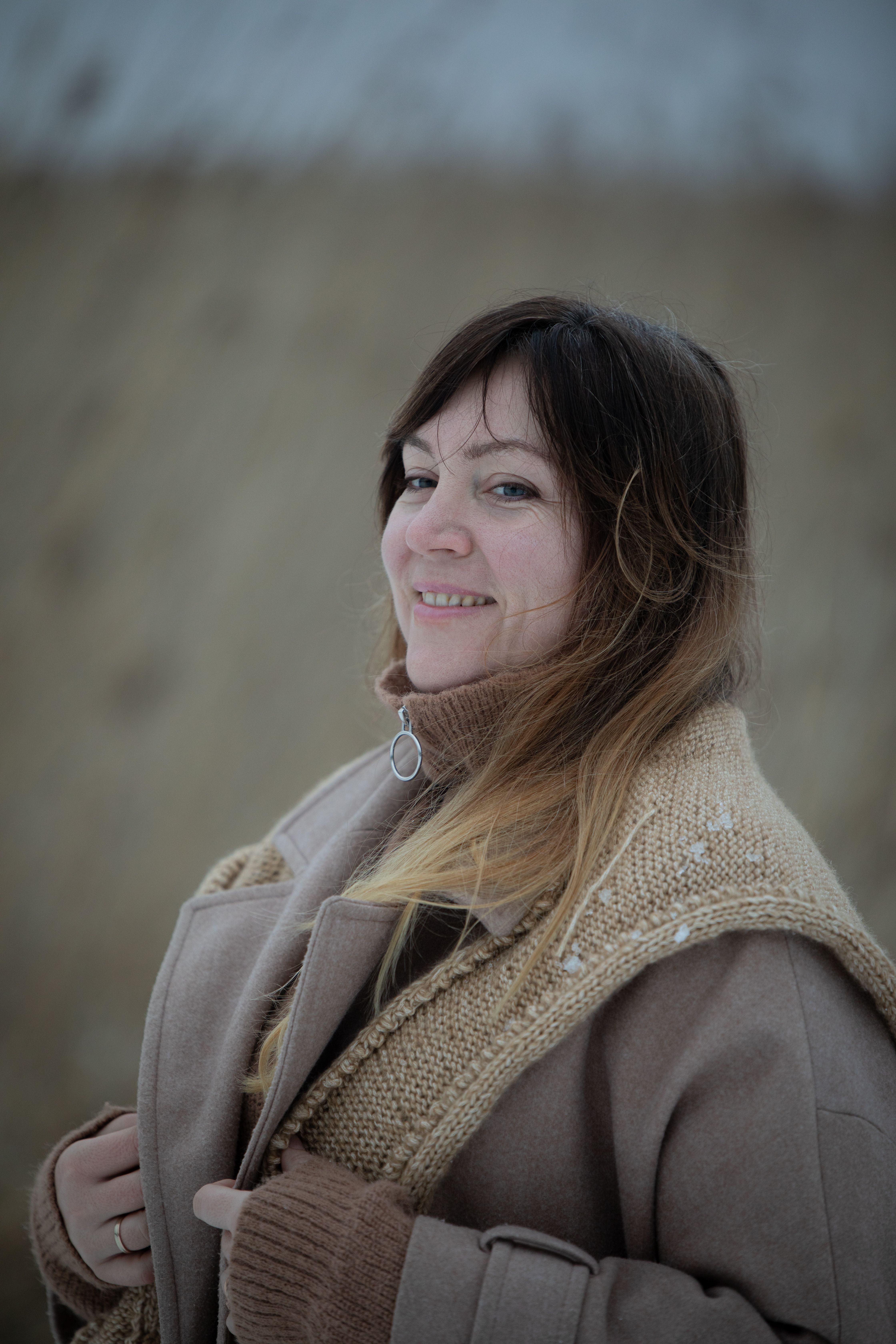 A smiling woman in a warm coat enjoying a cold day outdoors, exuding comfort and style.