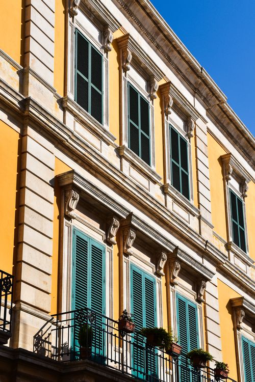 Free Elegant Italian building facade with colorful shutters and classic design elements under a clear blue sky. Stock Photo