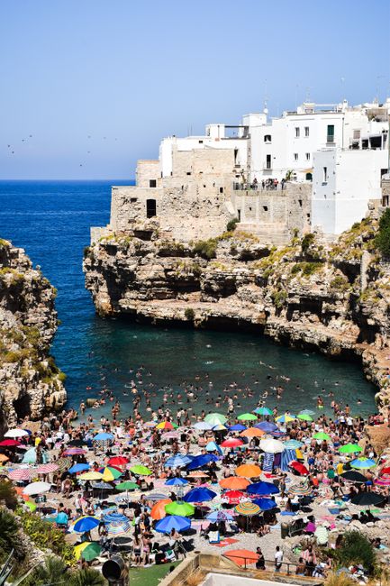 Vibrant beach scene at Polignano a Mare, Italy with colorful umbrellas and iconic cliffs.