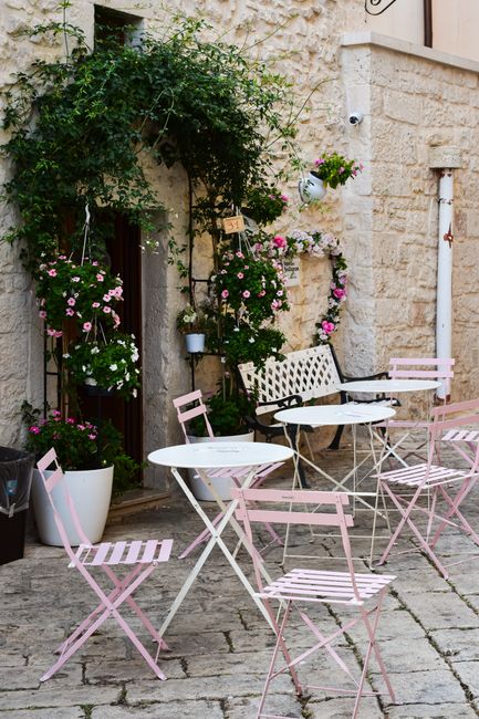 Cozy Italian courtyard featuring pink chairs and floral decor, perfect for a serene travel experience.