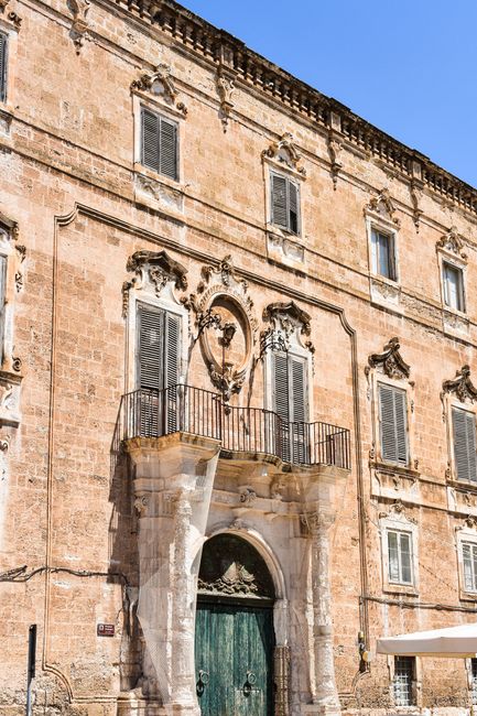 Historic stone facade showcasing Italian Baroque architecture with ornate details and blue sky.