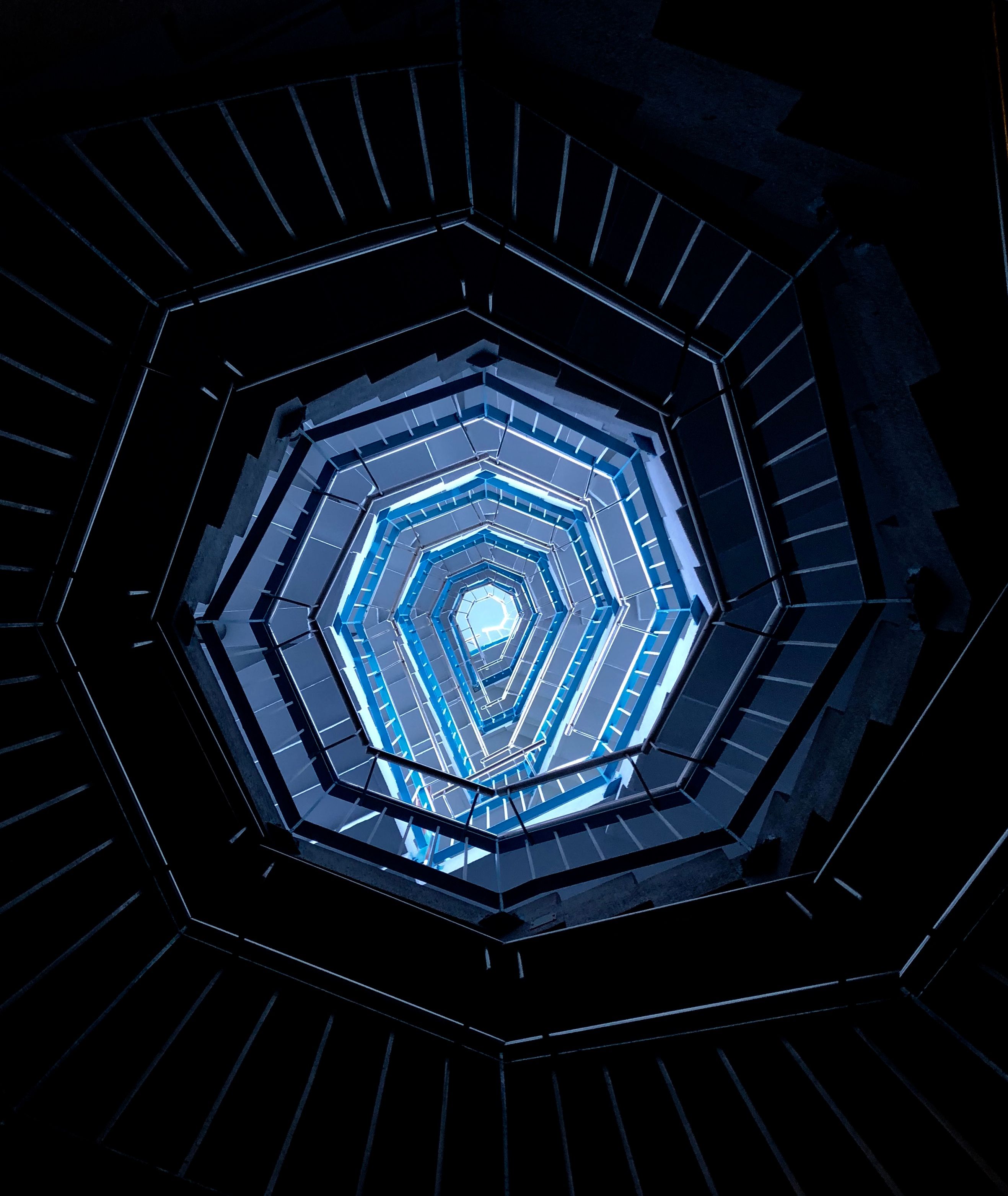 Upward view of a spiral staircase showing a hexagonal pattern in cool blue tones.