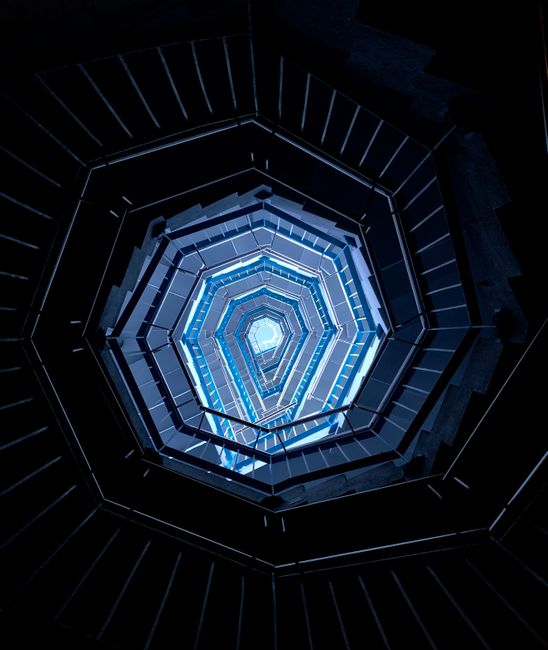 Upward view of a spiral staircase showing a hexagonal pattern in cool blue tones.