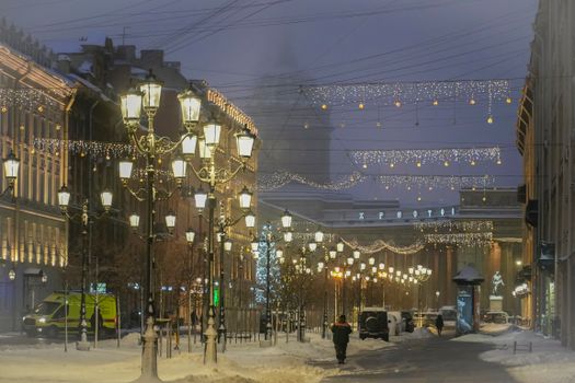 Snowy street in Saint Petersburg adorned with festive lights and glowing lampposts during winter night.
