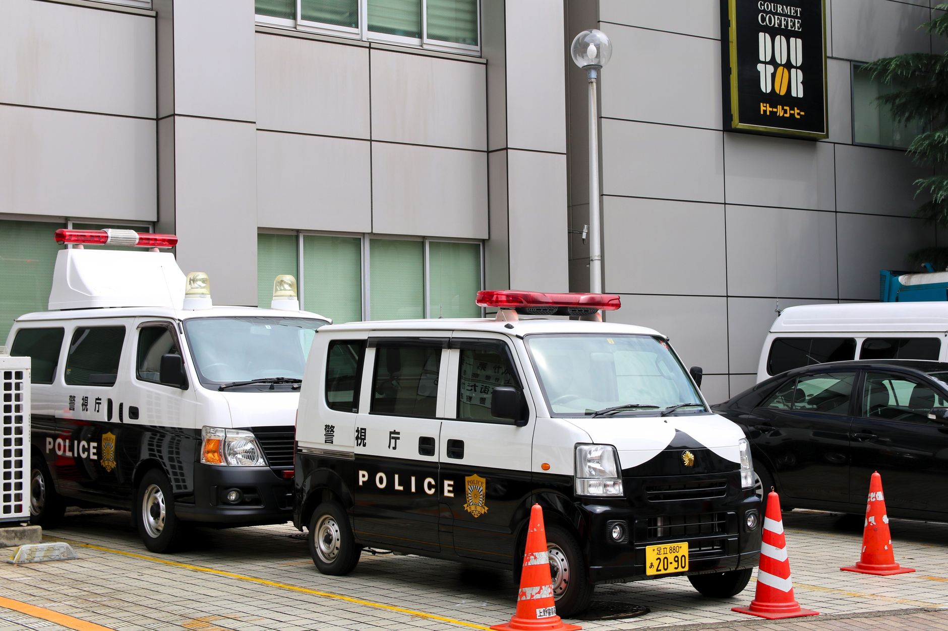 Police vans in Tokyo, Japan, parked outside a building with traffic cones.