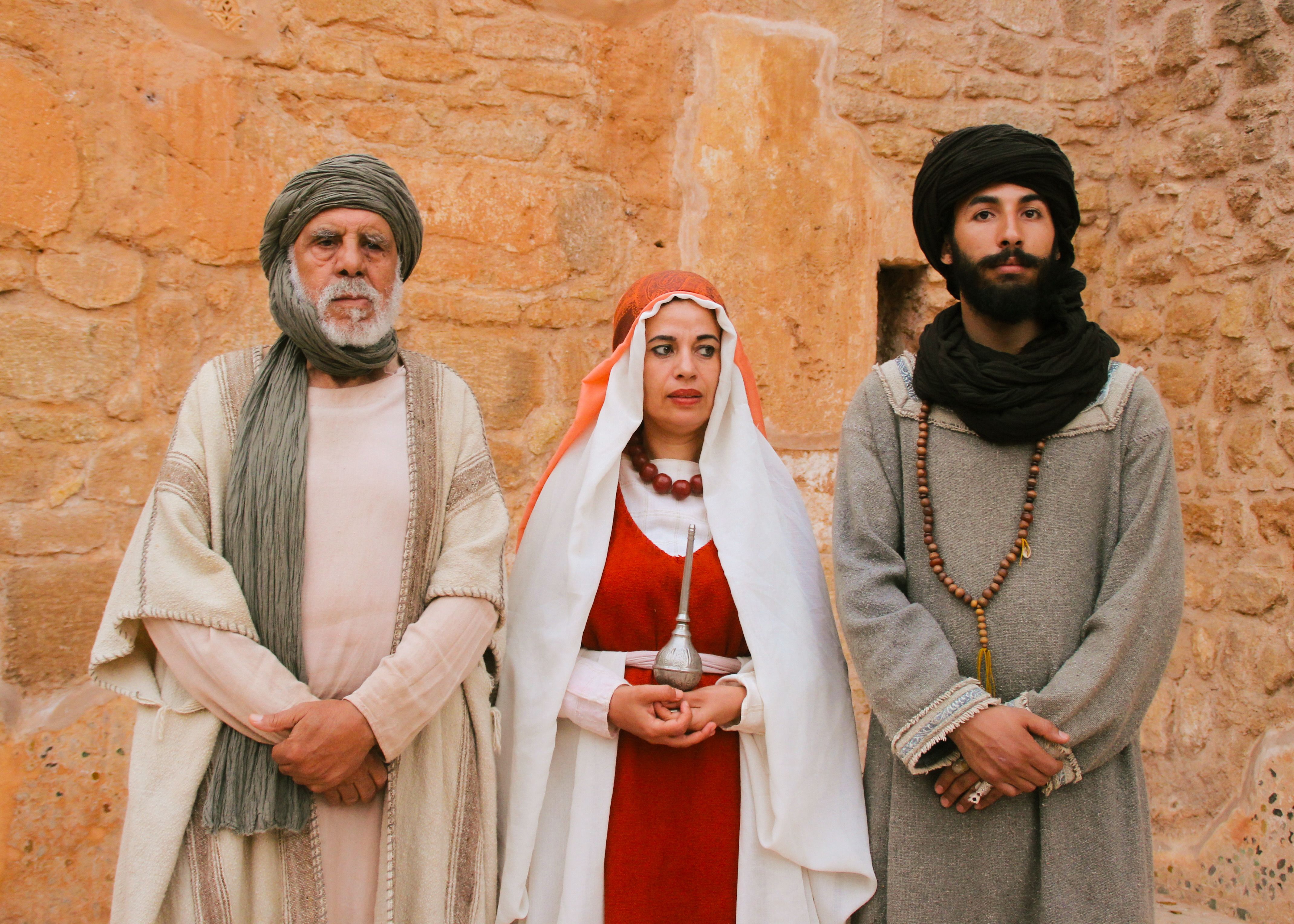 Gratis Tre persone in abiti tradizionali marocchini sono in piedi contro un antico muro di pietra, a testimonianza del loro patrimonio culturale. Foto a disposizione