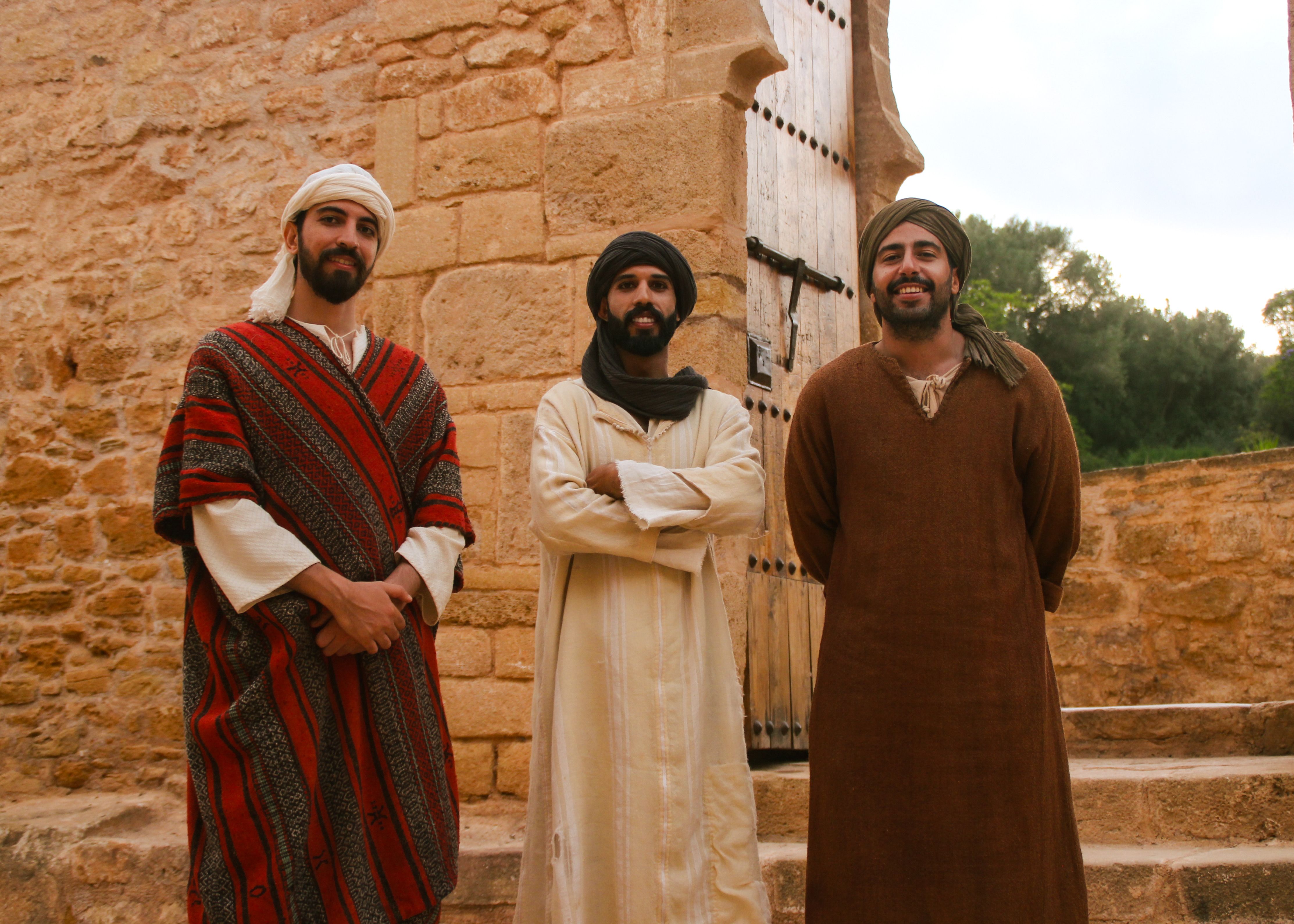 Gratis Tre uomini in abiti tradizionali marocchini stanno davanti a un'antica fortezza in pietra, simbolo del patrimonio culturale. Foto a disposizione