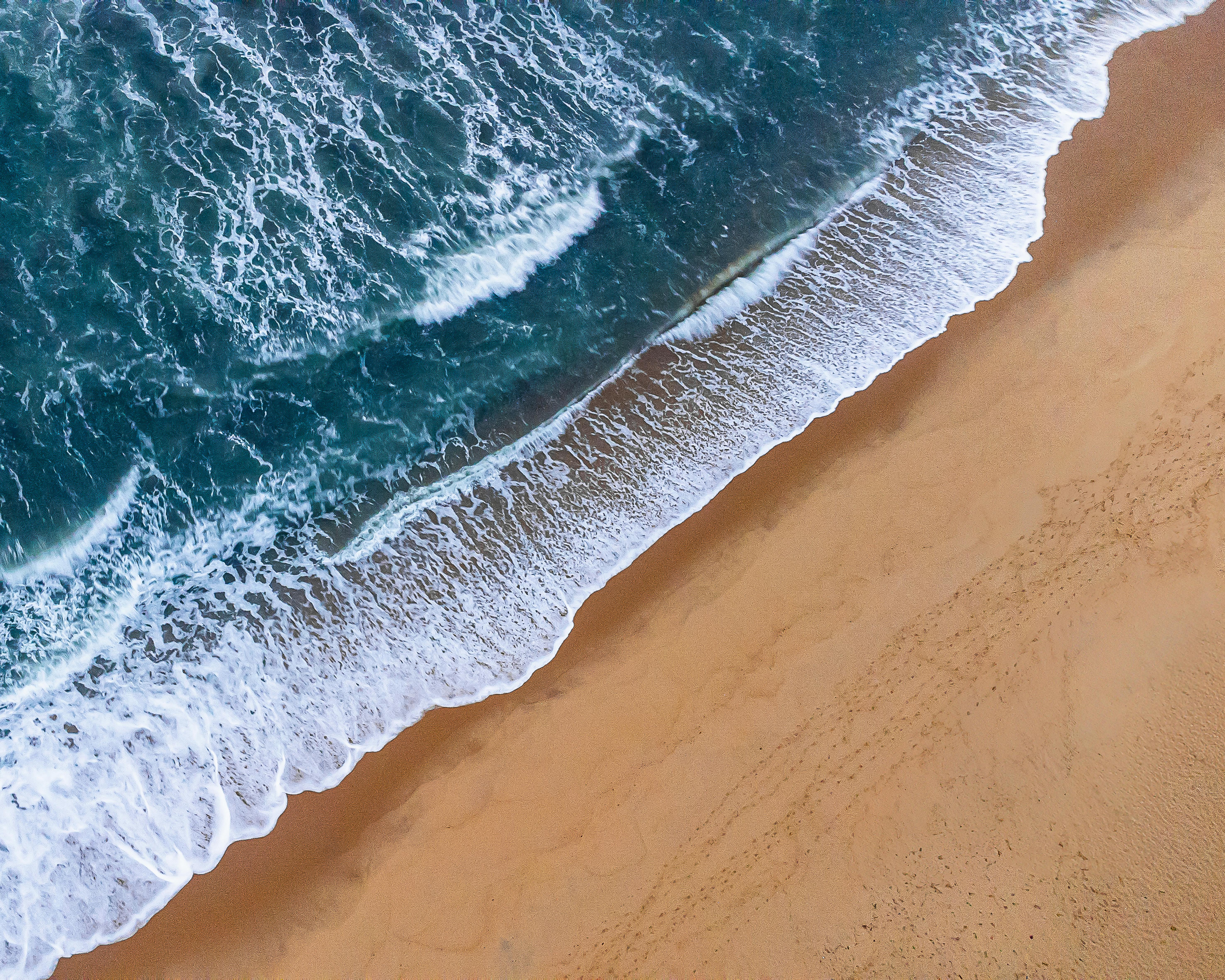 Stunning aerial view of ocean waves cascading onto the sandy beach in Ubatuba, São Paulo, Brazil.