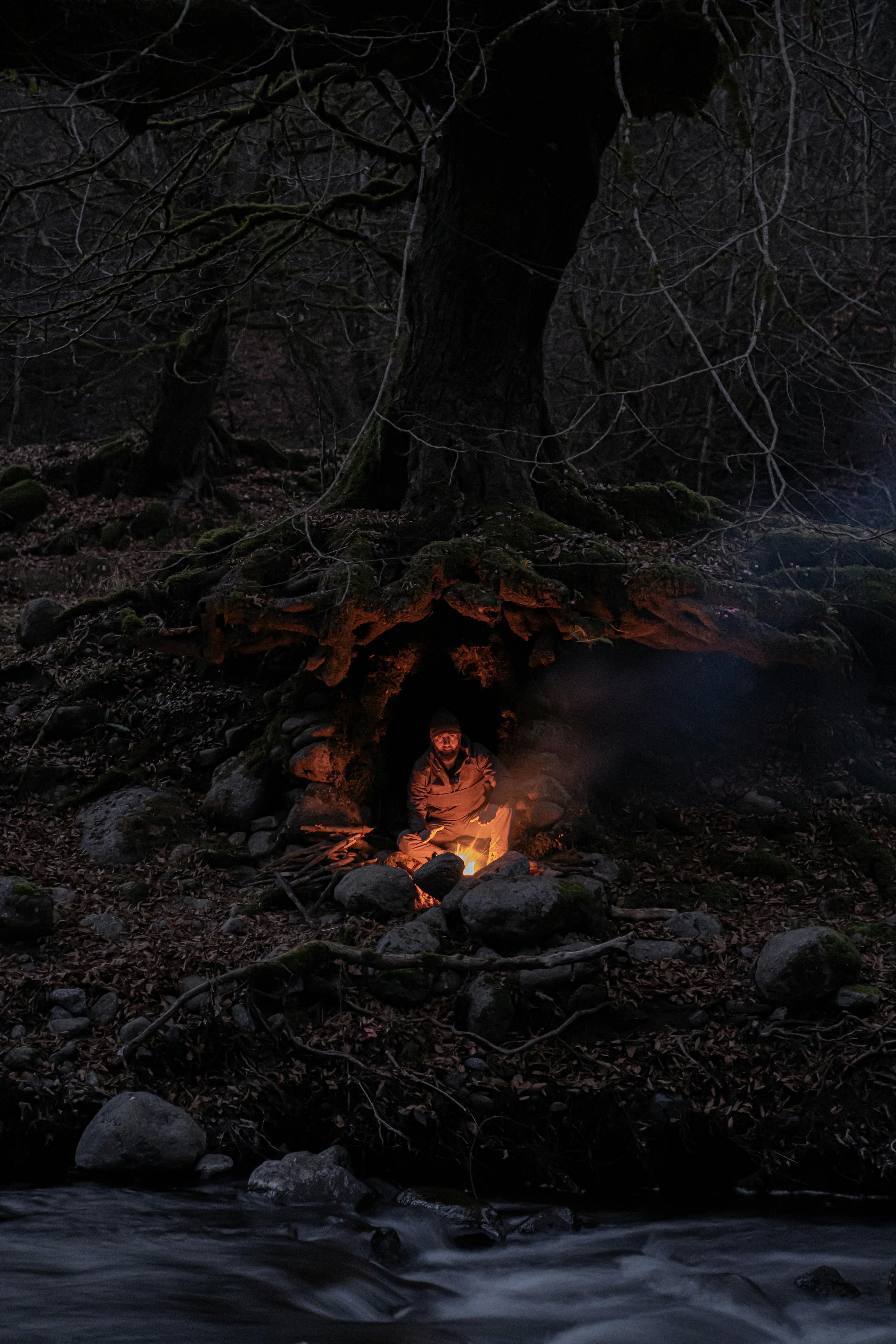 A person sitting by a campfire in a forest cave, creating a mystical night atmosphere.