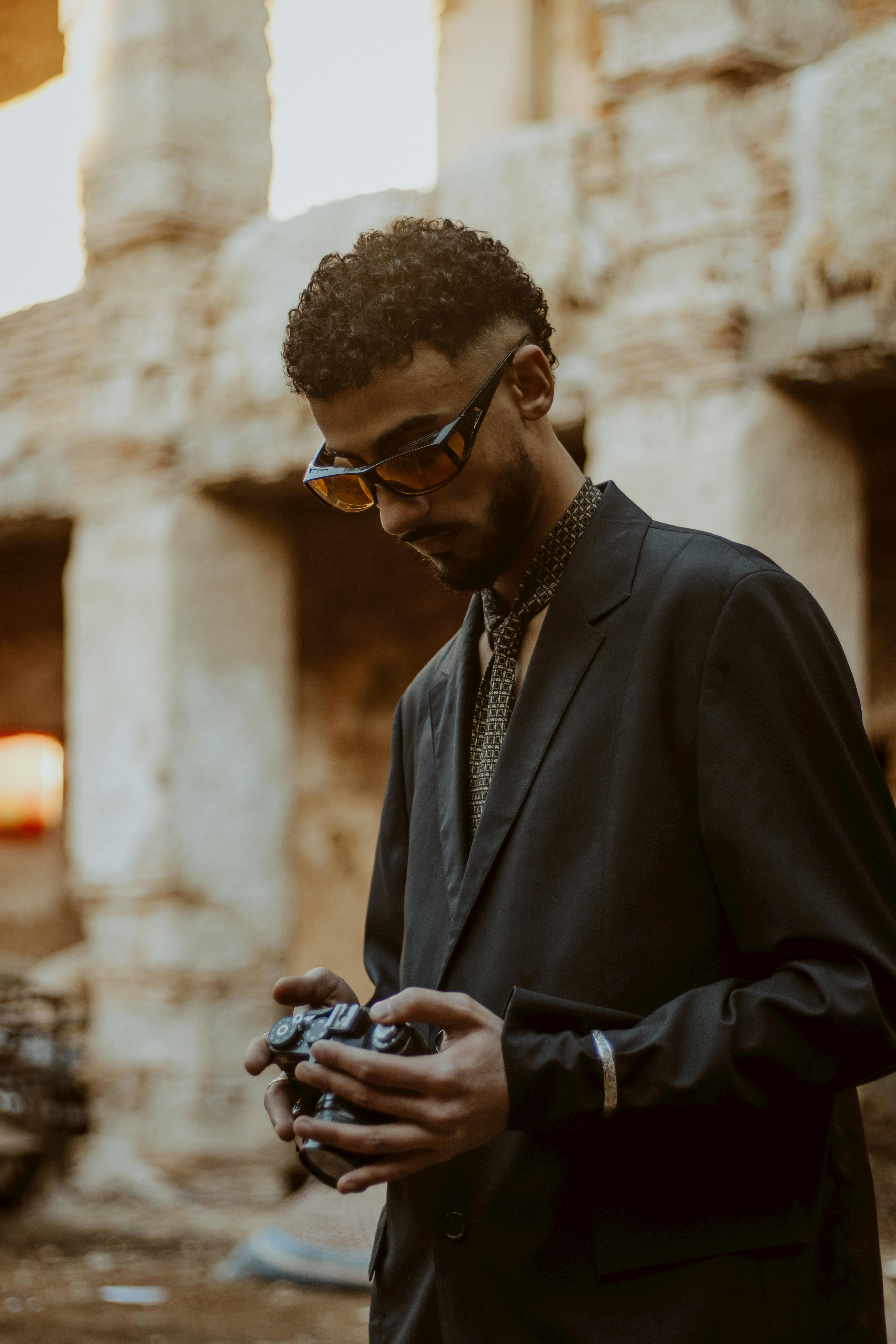 Vintage-styled man in suit holding camera in rustic outdoor setting.