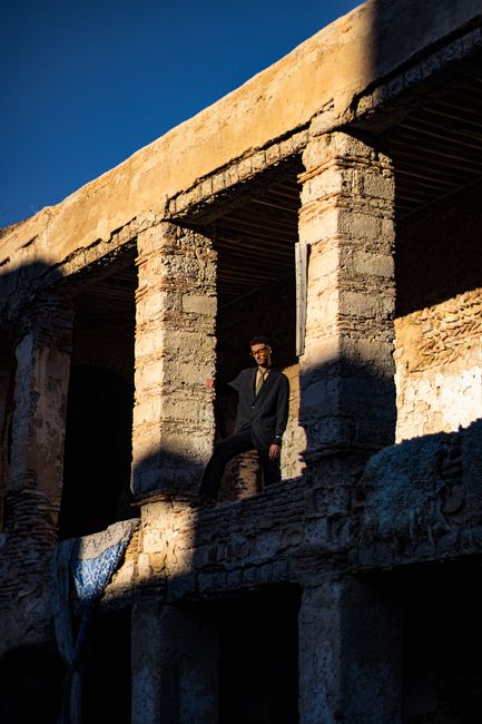 Man standing in a shadowed, aged building exterior, showcasing historic decay.