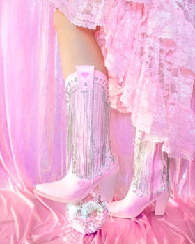 Pink cowboy boots with fringes and a disco ball on a pastel pink backdrop.