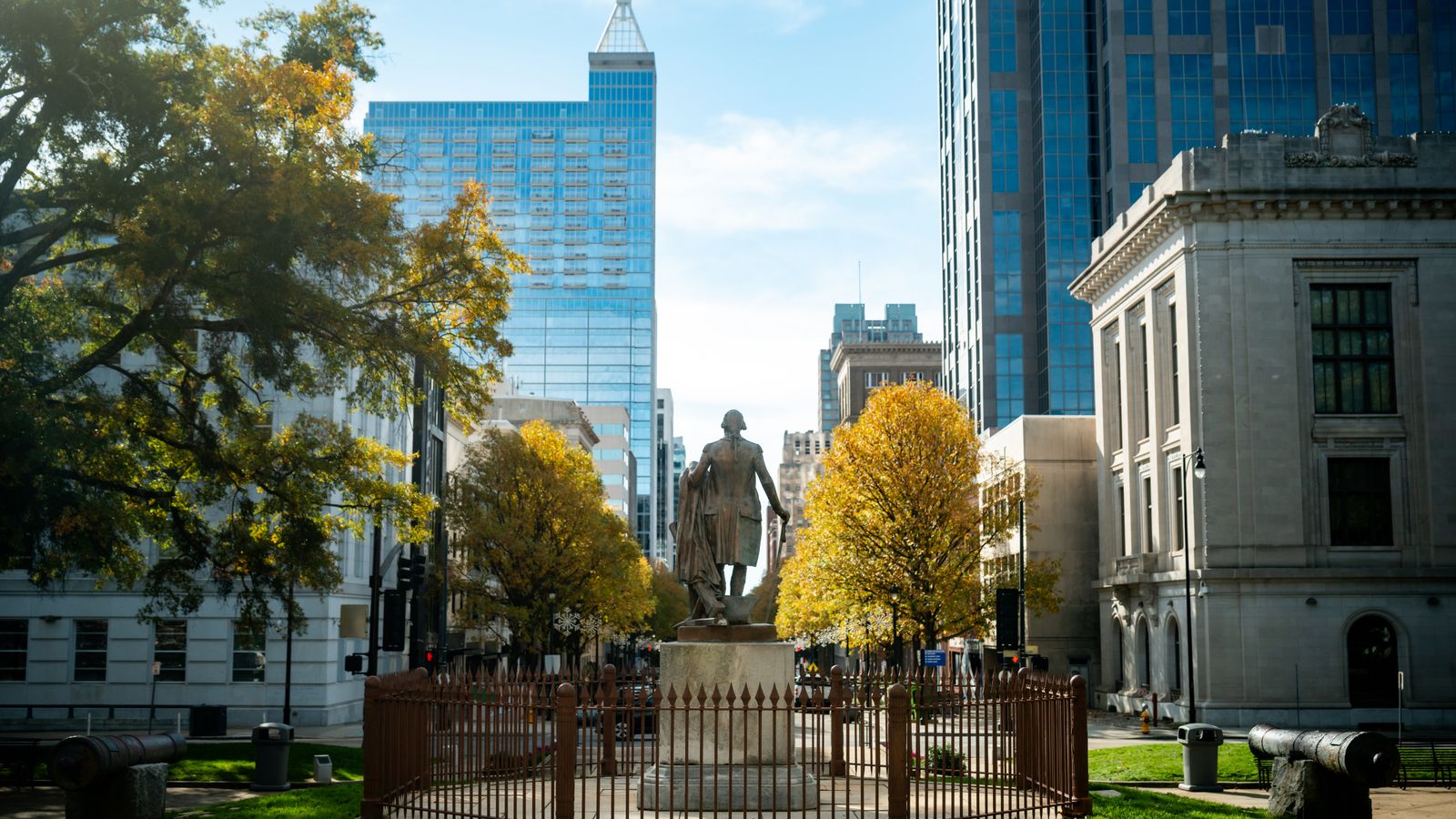 Statue in downtown Raleigh with skyscrapers and fall foliage.