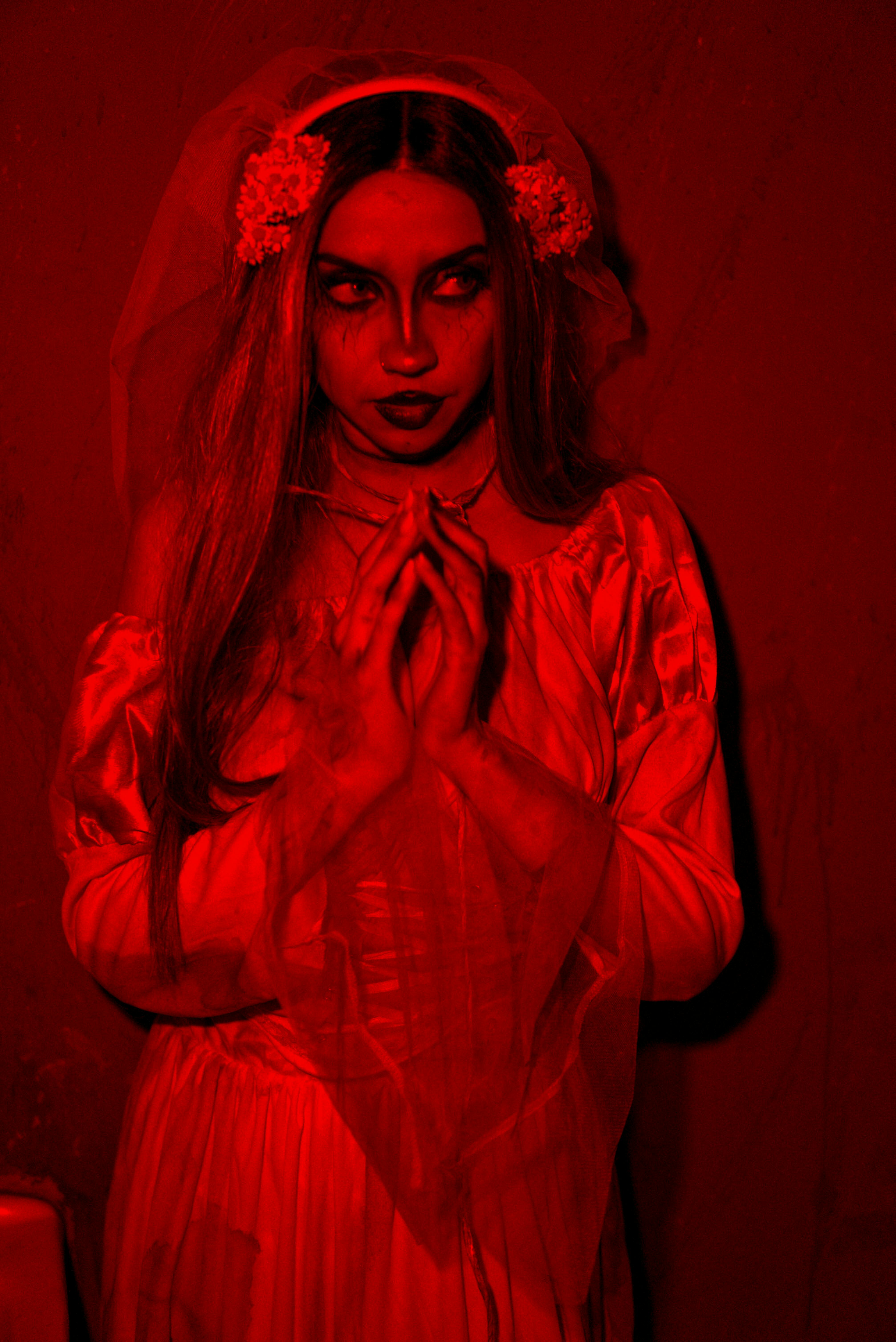 Eerie portrait of a woman in bridal attire, bathed in haunting red light.
