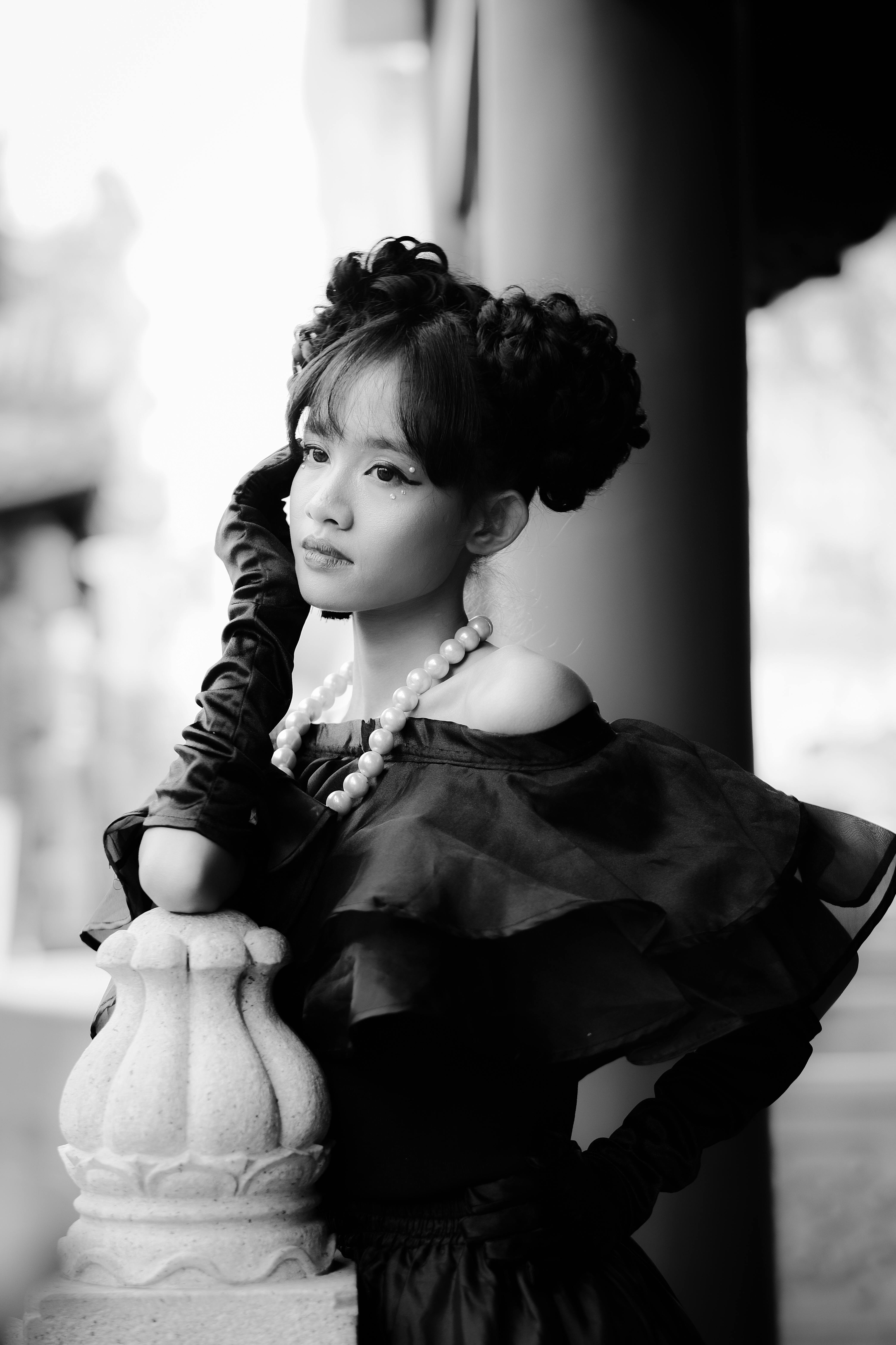 Black and white portrait of a young woman in vintage attire with pearl necklace, showcasing elegance.