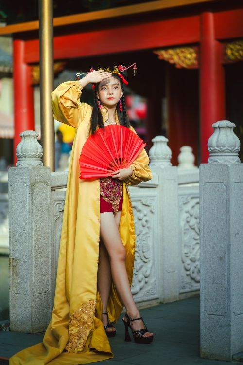 Free Woman in traditional Asian attire holding red fan, posing in cultural setting. Stock Photo