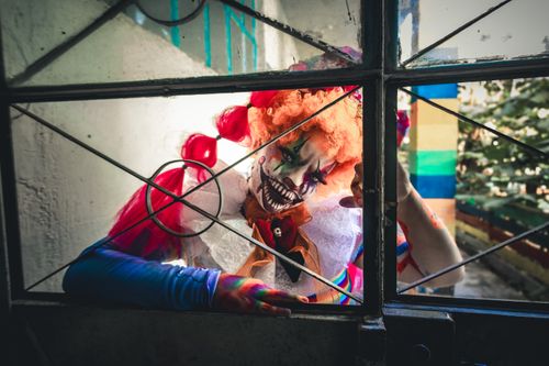 Free A frightening clown peering through a window with elaborate horror makeup. Stock Photo