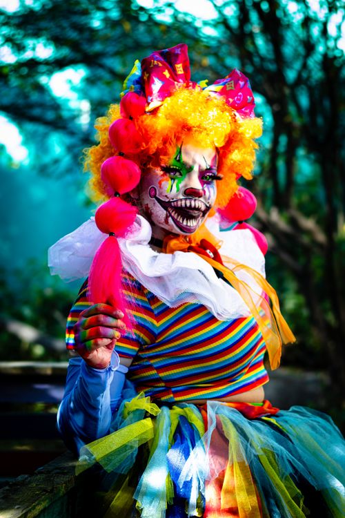 Free Colorful clown with dramatic makeup in a forest setting, creating a horror theme. Stock Photo