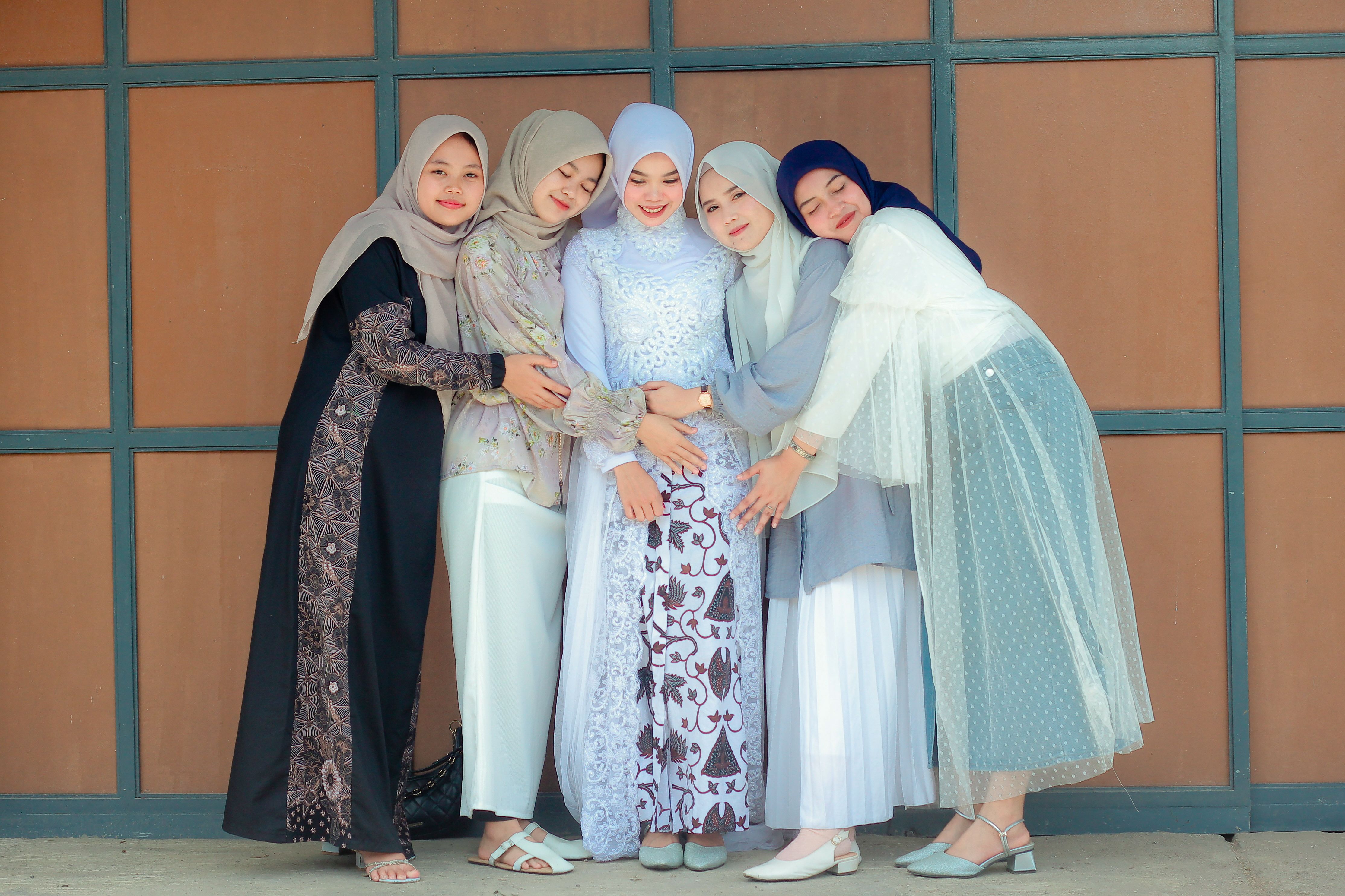 Five women in colorful traditional attire and hijabs posing closely together, symbolizing friendship.