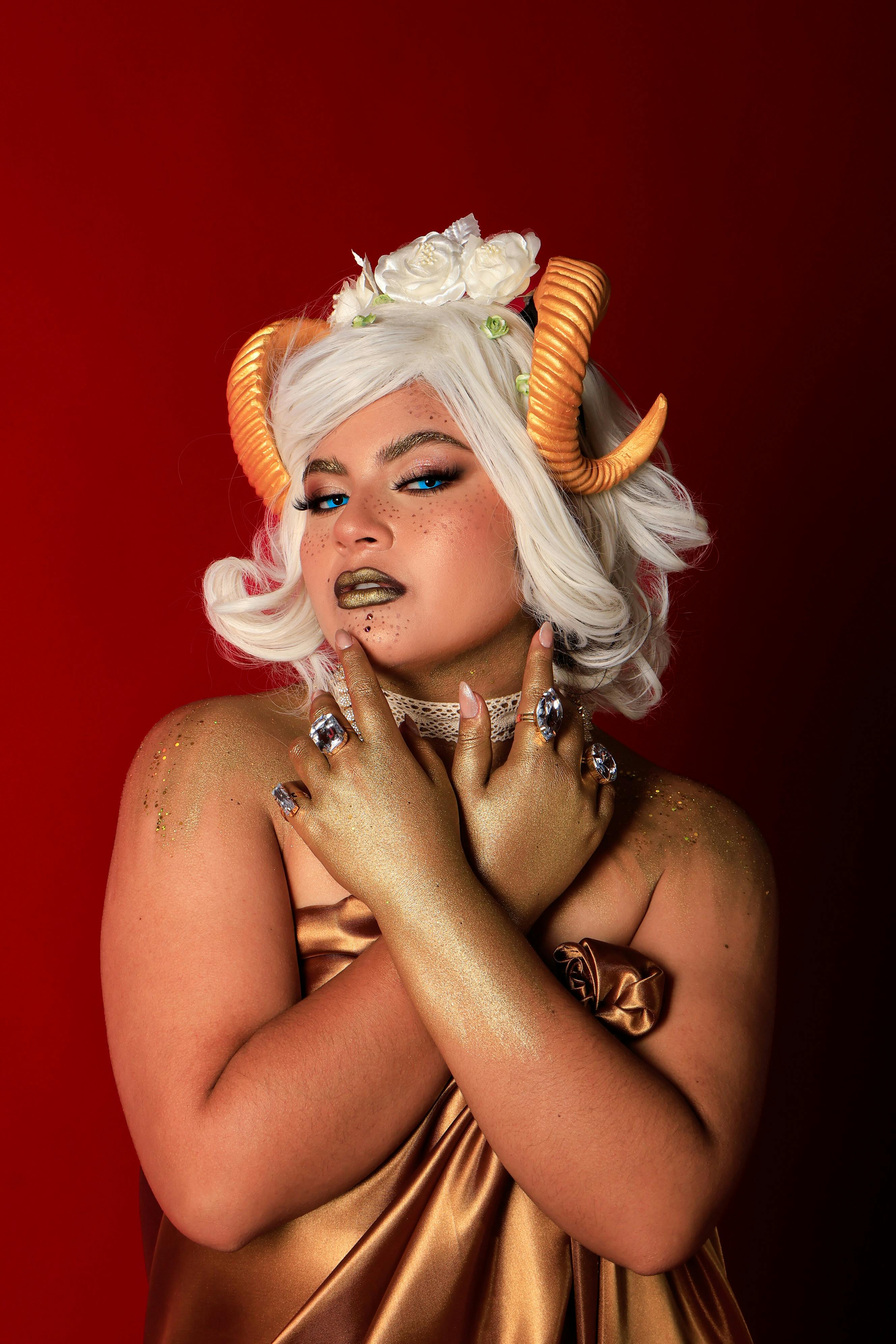 Gratuit Portrait fantastique saisissant d'une femme aux cheveux blancs, aux cornes orange et au maquillage doré sur fond rouge. Photos