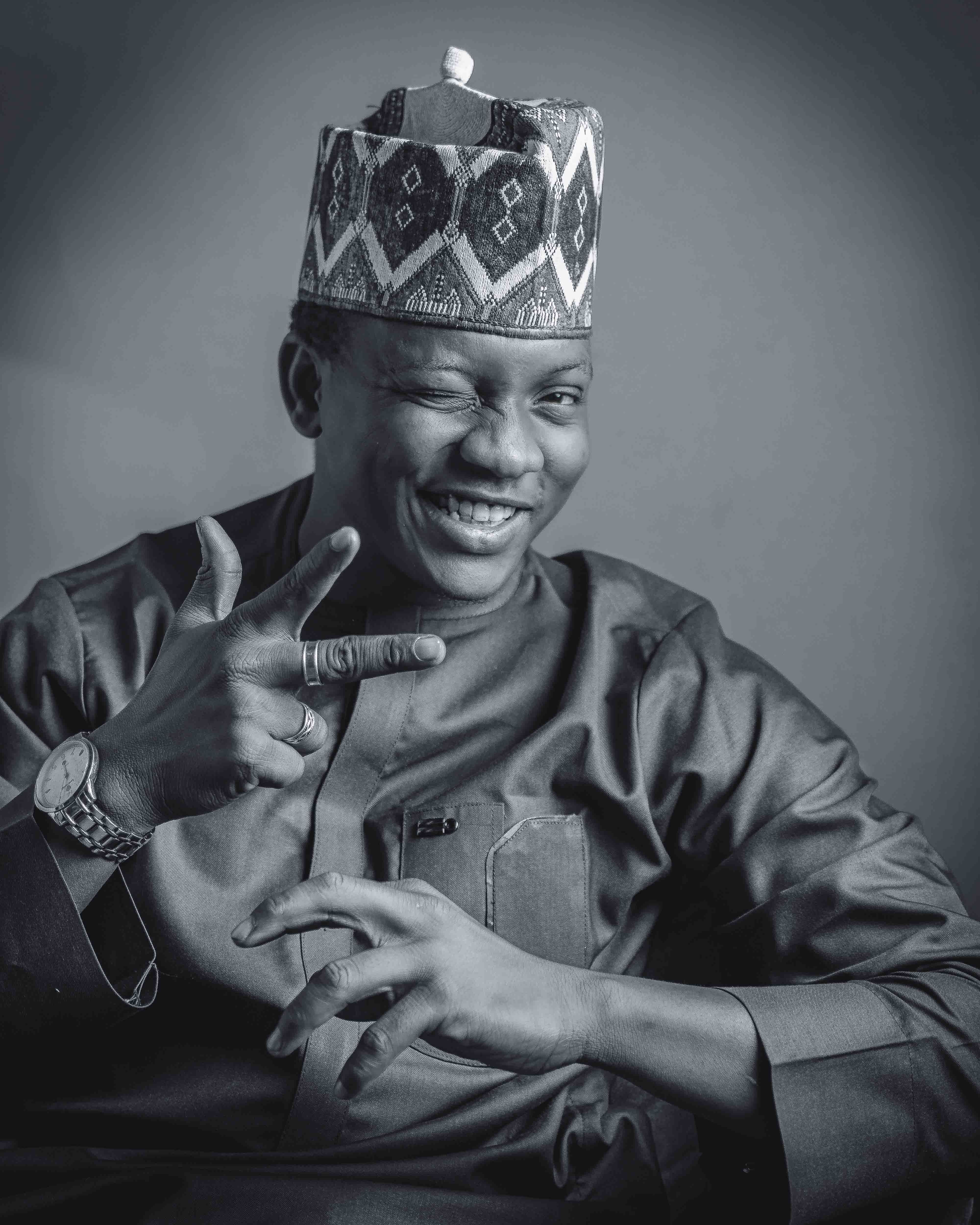 Black and white portrait of a smiling man in traditional African attire with a gesture.