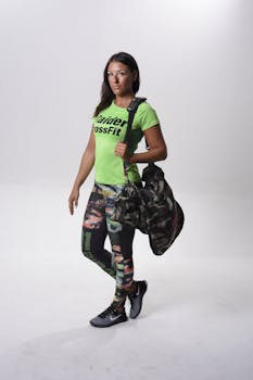 Athletic woman in vibrant gym clothes posing with a camo duffel bag against a clean background.