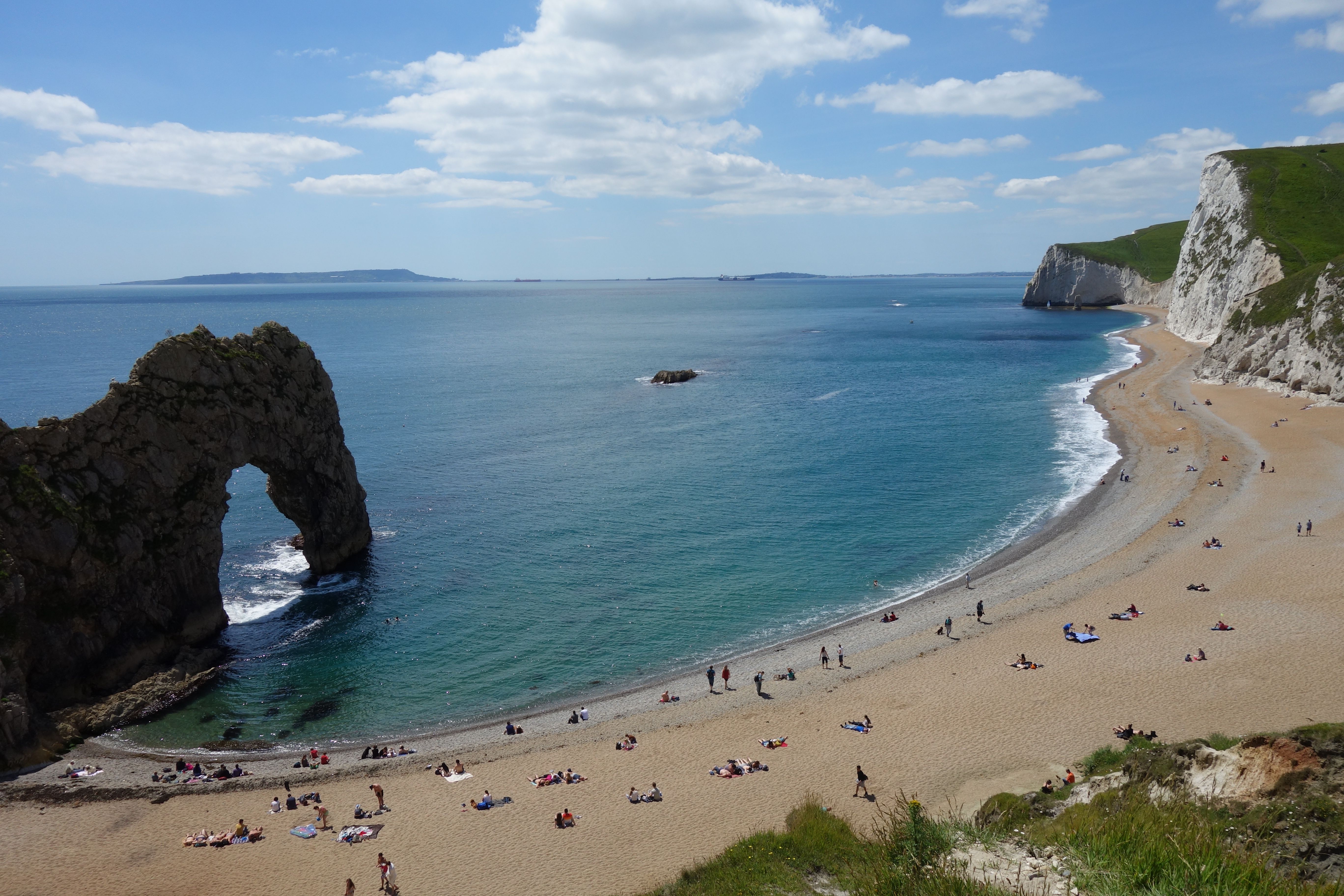 Breathtaking view of Durdle Door beach with sunbathers on a sunny day.