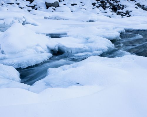 Free A tranquil winter scene of a frozen river surrounded by pristine snow, creating a peaceful ambiance. Stock Photo