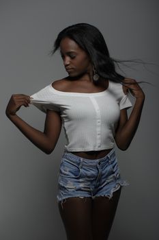 Stylish portrait of a woman in a white crop top and denim shorts set against a neutral background.