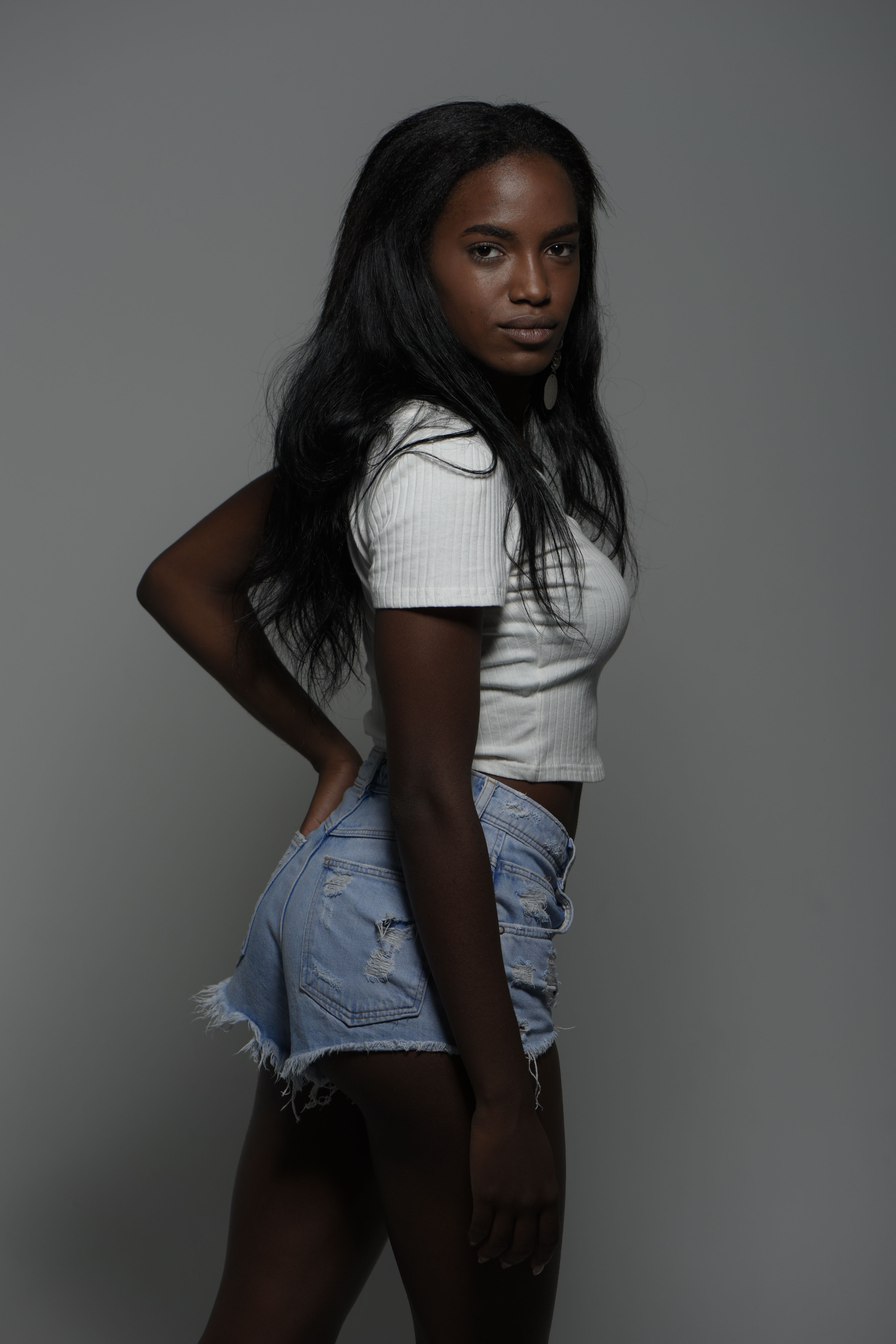 Young woman in casual outfit posing confidently against a neutral backdrop.