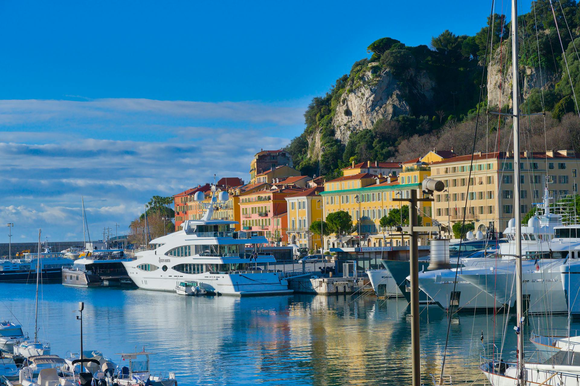 Colorful harbor scene in Nice, France, featuring luxury yachts and historic buildings under a bright blue sky.