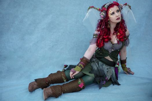 Captivating fairy with red hair and floral costume in an ethereal setting.