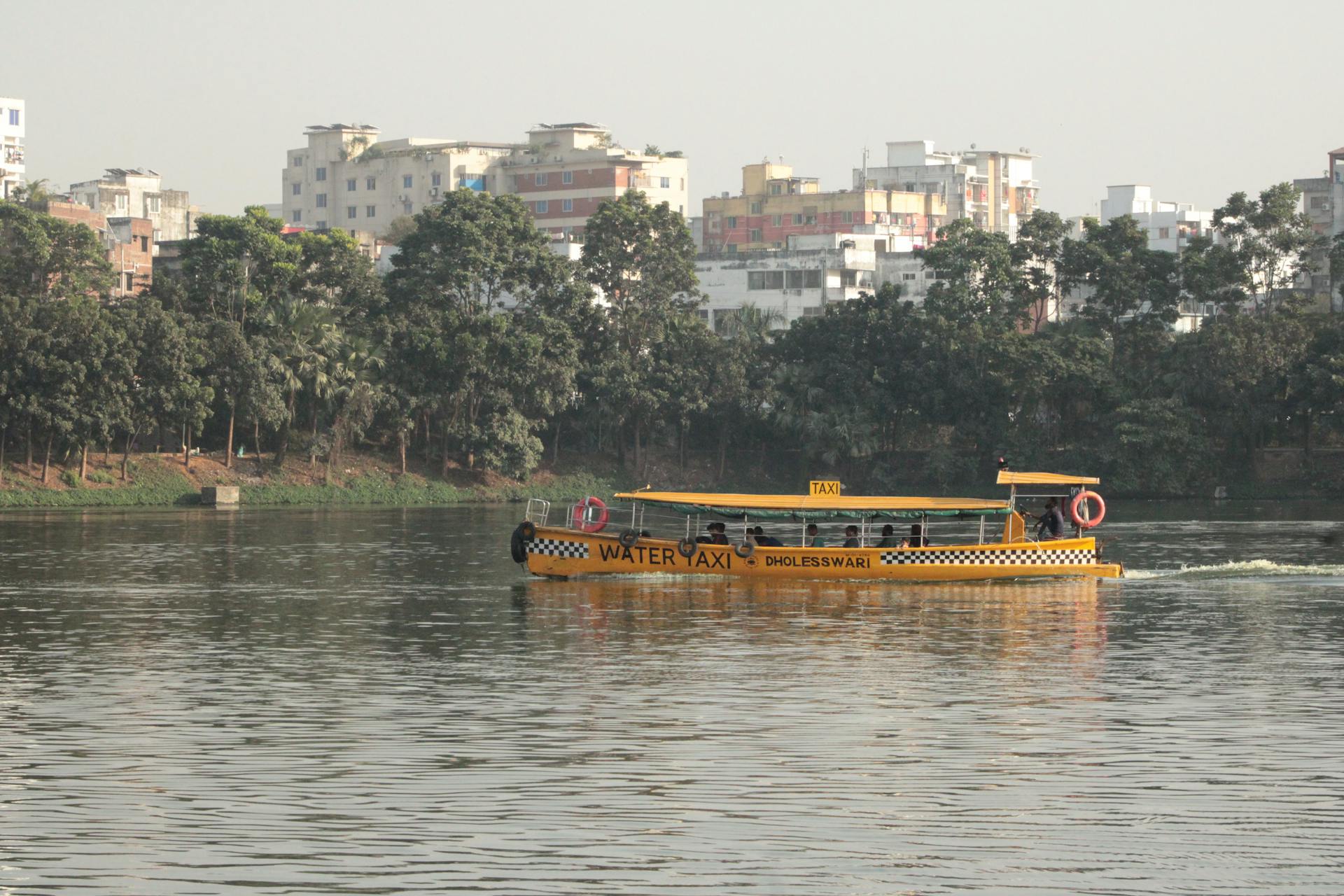 A yellow water taxi cruising on a river in an urban area with buildings in the background.