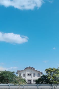 A modern house set against a vibrant blue sky with fluffy clouds and greenery.