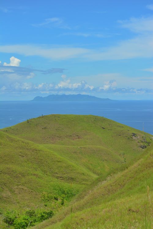 Free Beautiful green hills with a background of ocean and distant islands under a clear blue sky. Stock Photo